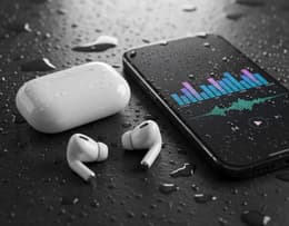 AirPods Pro 3 on a wet surface beside an iPhone.