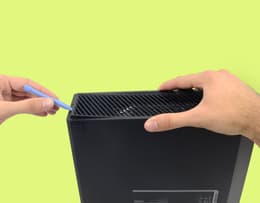A person using a pry tool to remove the Xbox One left-side vent panel
