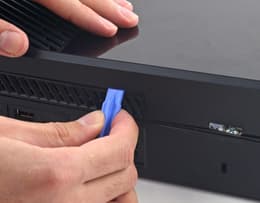 Xbox One face down with a pry tool inserted into the console seam to begin prying open the panels